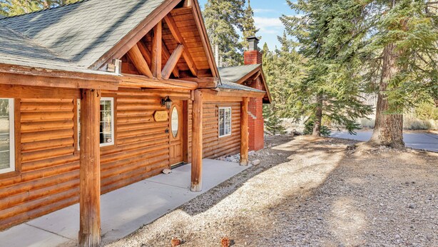 Une cabane en rondins avec un toit en pente, une cheminée et une allée gravillonnée.