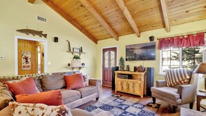 Un salon chaleureux avec un plafond en bois, un ensemble de canapés, un tapis à motifs et un meuble en bois contenant du matériel audio.
