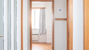 A hallway with a wooden door frame, a tiled floor, and a view into a room with a bed and a window with curtains. - The Holiday House ÁSAR - Amazing View (Kirkjubæjarklaustur)
