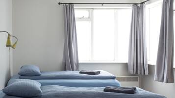 Une chambre avec deux lits, une fenêtre avec des rideaux, un radiateur et une lampe fixée au mur.