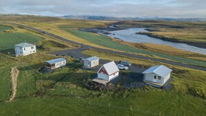 A remote, rural landscape with several small, white buildings with red roofs, surrounded by green fields and a winding road. - The Holiday House ÁSAR - Amazing View (Kirkjubæjarklaustur)