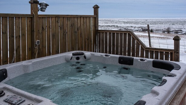 A hot tub on a wooden deck with a view of a snowy beach. - The Holiday House ÁSAR - Amazing View (Kirkjubæjarklaustur)