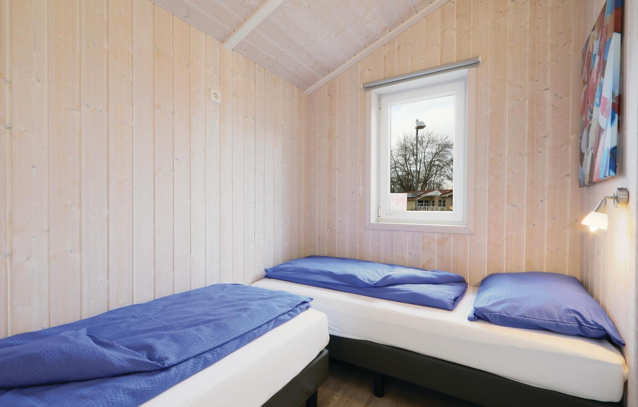 Eine kleine, einfache Blockhütte mit zwei Betten, einem Fenster mit Blick auf ein Haus und einem Bild an der Wand.