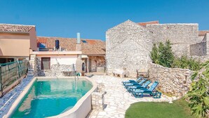 Una piscina envoltada per parets de pedra, amb gandules i un edifici de pedra al fons.