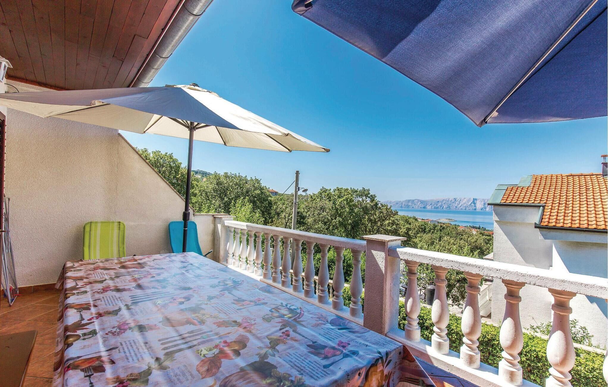 A balcony with a table covered in a floral tablecloth, a green chair, and a large umbrella.