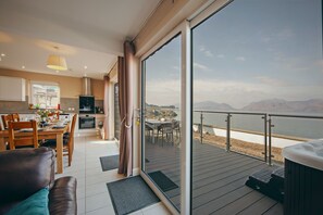 A modern kitchen with a dining area and a sliding glass door leading to a deck with a view of a lake and mountains. - Beach House 3 with Hot Tub - sleeps 9 guests  in 4 bedrooms (Appin)