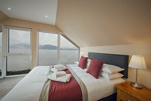 A hotel room with a large bed, a nightstand, a lamp, and a view of a body of water through the windows. - Beach House 3 with Hot Tub - sleeps 9 guests  in 4 bedrooms (Appin)