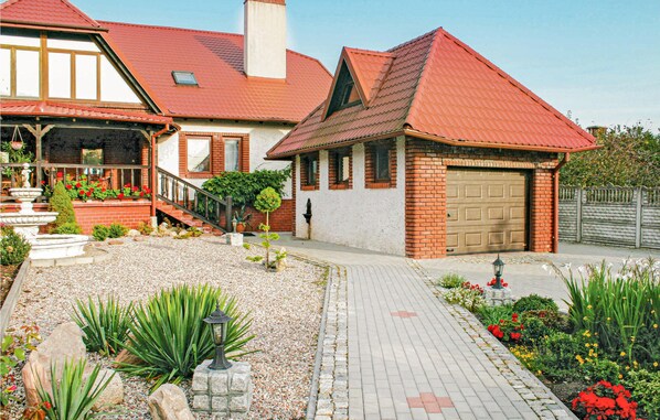 A two-story house with a red roof, a brick exterior, and a front garden with a pathway.
