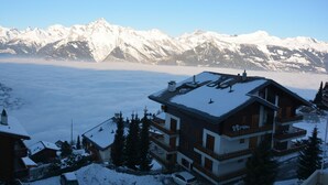 Un edificio de varios pisos con balcones, rodeado de montañas nevadas y un cielo despejado.