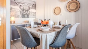 Un comedor con una mesa dispuesta para cuatro personas, rodeada de sillas grises tapizadas. Un cuadro grande con la imagen de un yakadorno la pared, y hay tres individuales tejidos sobre la mesa.