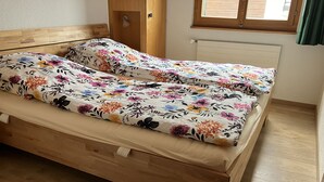 Ein hölzernes Bett mit floraler Bettwäsche in einem Raum mit Holzboden und einem Fenster mit Vorhängen.