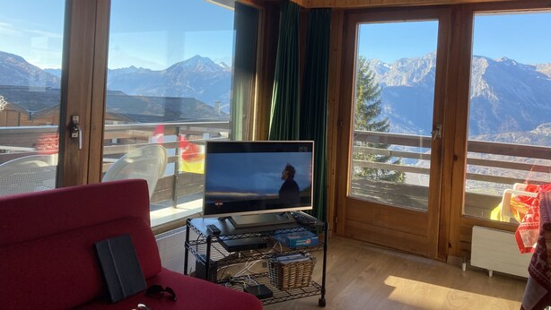 Ein Zimmer mit einem großen Fernseher auf einem Schrank, einem roten Sofa und Bergblick durch große Fenster.