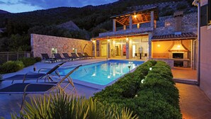 A poolside area with lounge chairs, a stone wall, and a stone building with a fireplace. - Awesome home in Trsteno with sauna (Trsteno)