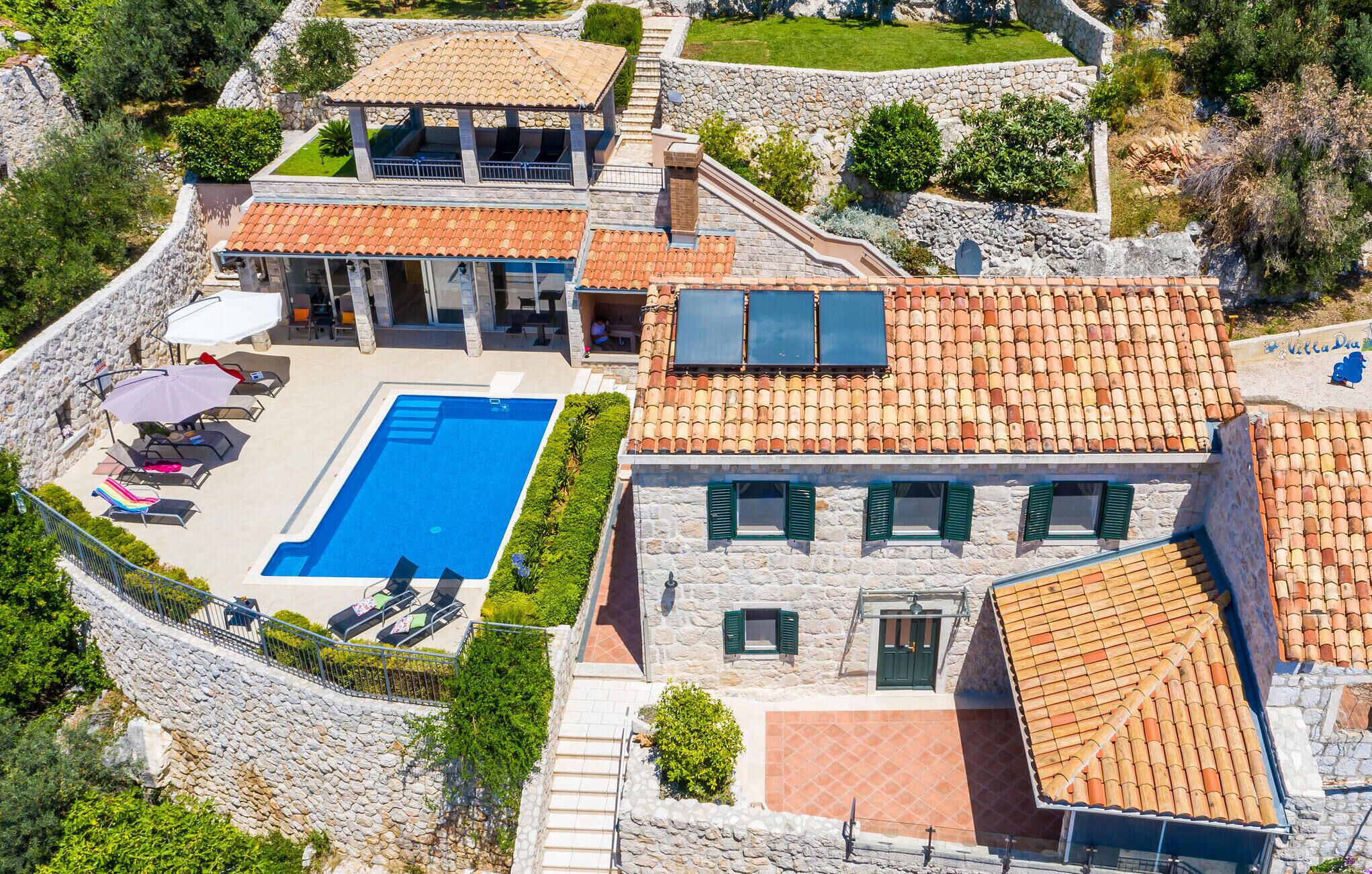 A villa with a swimming pool, stone walls, and a tiled roof.