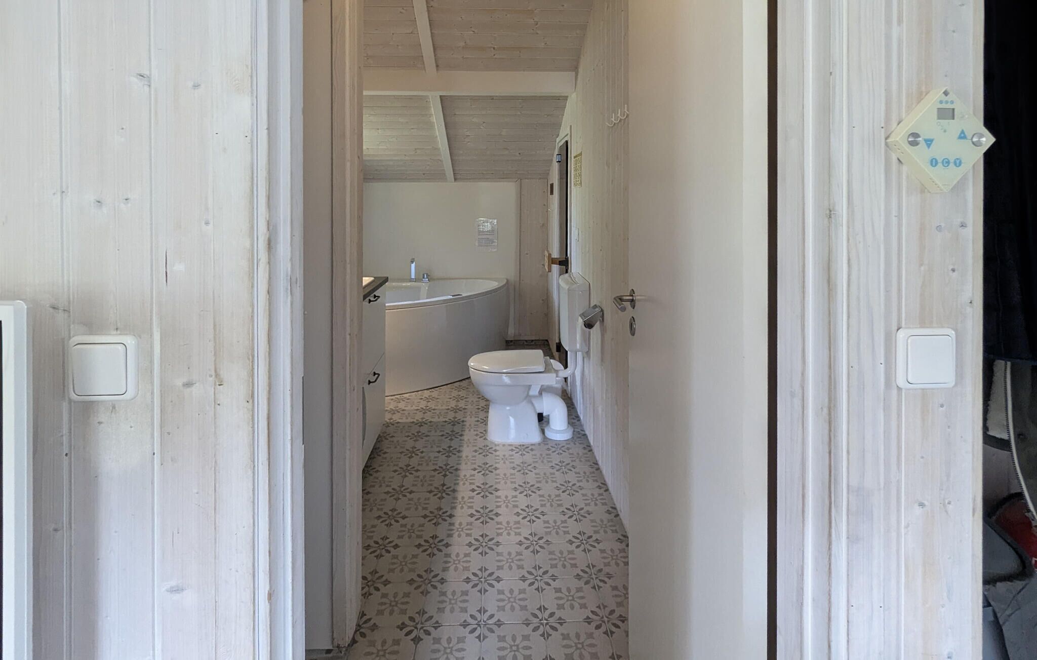 A narrow hallway leading to a bathroom with a toilet, sink, and patterned floor tiles.