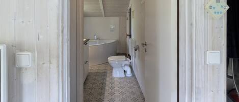 A narrow hallway leading to a bathroom with a toilet, sink, and patterned floor tiles.