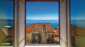 Uitzicht vanaf een balkon op een kustgebied met terracotta daken en een helderblauwe lucht.