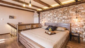 Een slaapkamer met een stenen muur, houten balken, een bed met een ontbijttafel en een trap.
