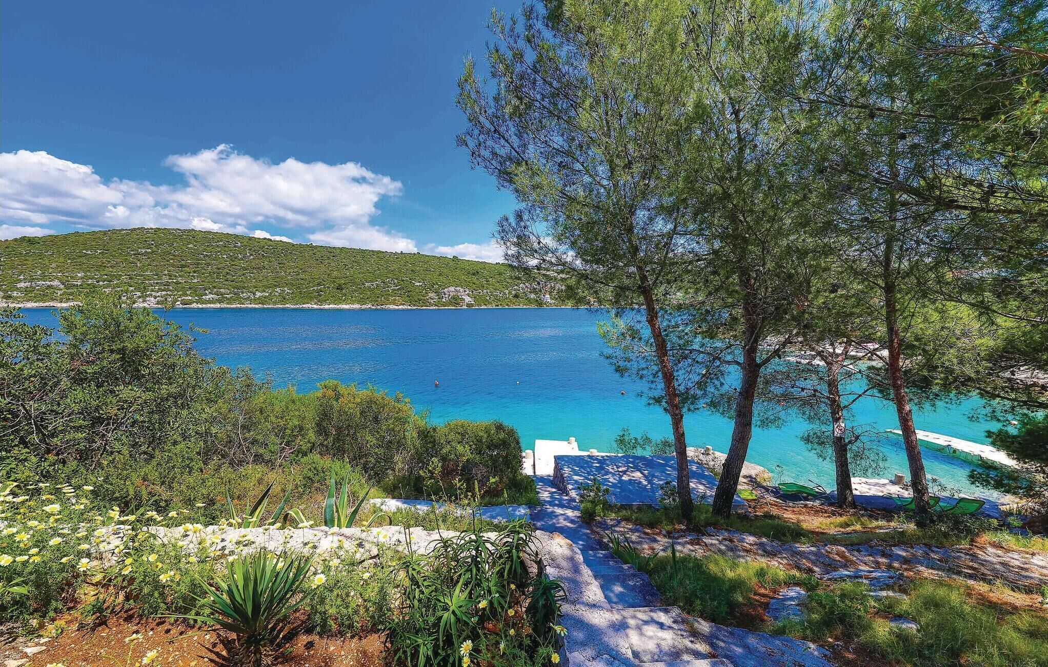Un paysage côtier avec une mer bleue et limpide, un sentier pavé de pierres et des arbres.