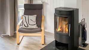 A modern living room with a wood-burning stove, a comfortable chair with a cushion, and a radiator. - Gorgeous home in Travemünde-Priwall (Travemünde-Priwall)