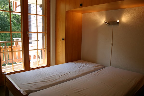 A room with two beds, wooden walls, and a large window with a view of the outside.