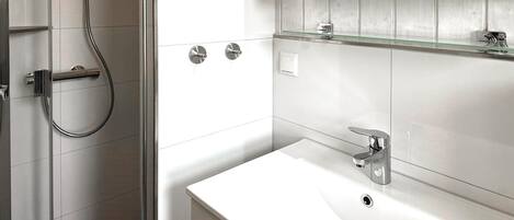 A modern bathroom with a white sink, chrome fixtures, and a glass shower enclosure.