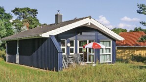 A small, single-story building with a sloped roof, a chimney, and a covered outdoor seating area with tables and chairs. - Frische Brise 17 - Dorf 3 (Travemünde-Priwall)