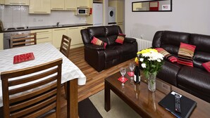 Una sala de estar moderna con comedor, un sofá de cuero negro y una cocina con armarios de tonos claros.