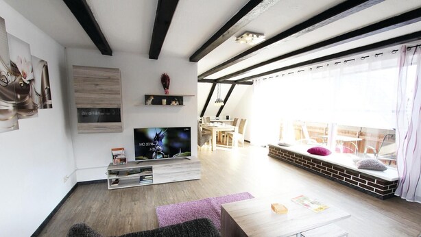 Een moderne woonkamer met een televisie, boekenkasten, een eethoek en uitzicht op de omgeving.