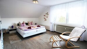 Een slaapkamer met een bed, twee nachtkastjes, een stoel, een radiator en een raam met gordijnen.