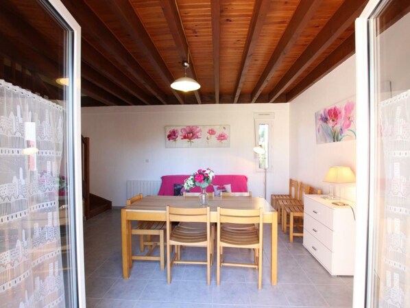 A cozy dining area with a wooden table and chairs, a pink sofa, and a white dresser with a lamp.