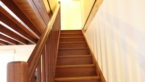 Una escalera de madera con barandilla, que lleva a un espacio interior luminoso.