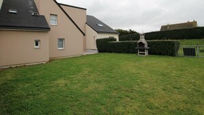 Un barrio residencial con dos casas, un césped y una parrilla de piedra.