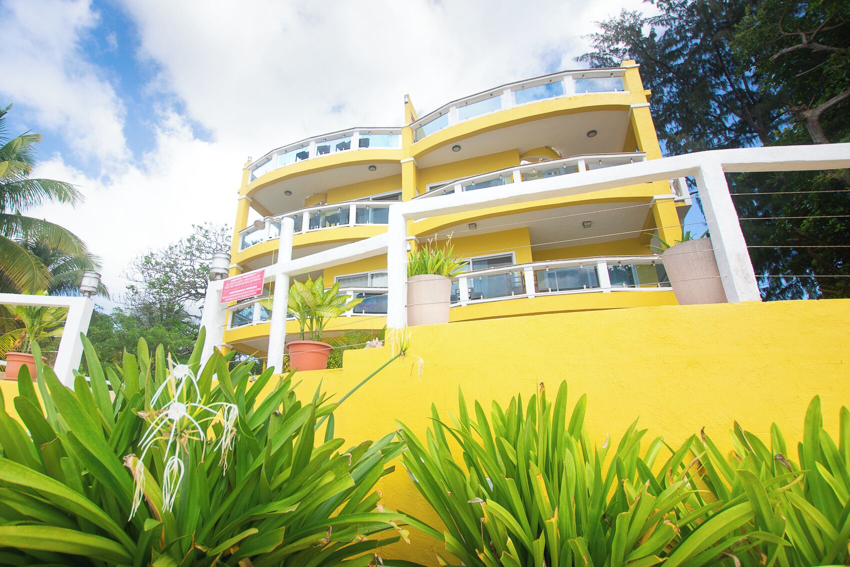 A multi-story yellow building with balconies, surrounded by lush greenery.
