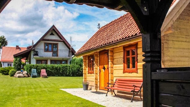 Een traditioneel houten huis met een rode dakbedekking, een houten veranda en een bankje.