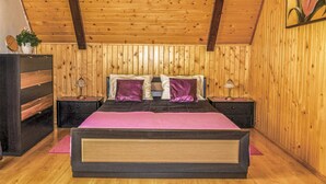 Een slaapkamer met houten lambrisering, een groot bed, twee nachtkastjes met lampen, een kaptafel en een wandklok.