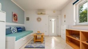 Ett kompakt bostadsutrymme med en säng, ett litet bord, en soffa och ett fönster.