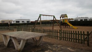 Un'area giochi con altalena e scivolo, circondata da una recinzione in legno e un tavolo da picnic.