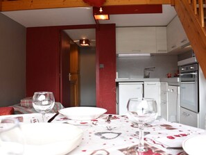 Ein Essbereich mit Tisch für zwei Personen, eine Küche im Hintergrund und eine Holztreppe.