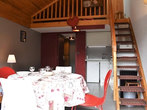 Uma sala de jantar com uma mesa posta para dois, uma cadeira vermelha e uma escadaria com degraus estampados.
