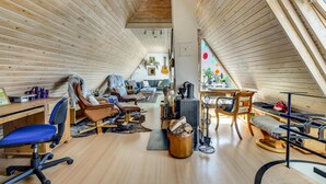A cozy, well-lit attic room with wooden slats on the ceiling, a dining area with a table and chairs, and a seating area with leather chairs and a blue office chair. - Amazing home in Haderslev (Haderslev)