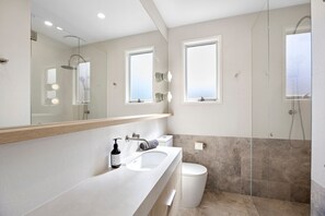 A modern bathroom with a large mirror, two sinks, a toilet, and a glass-enclosed shower area.