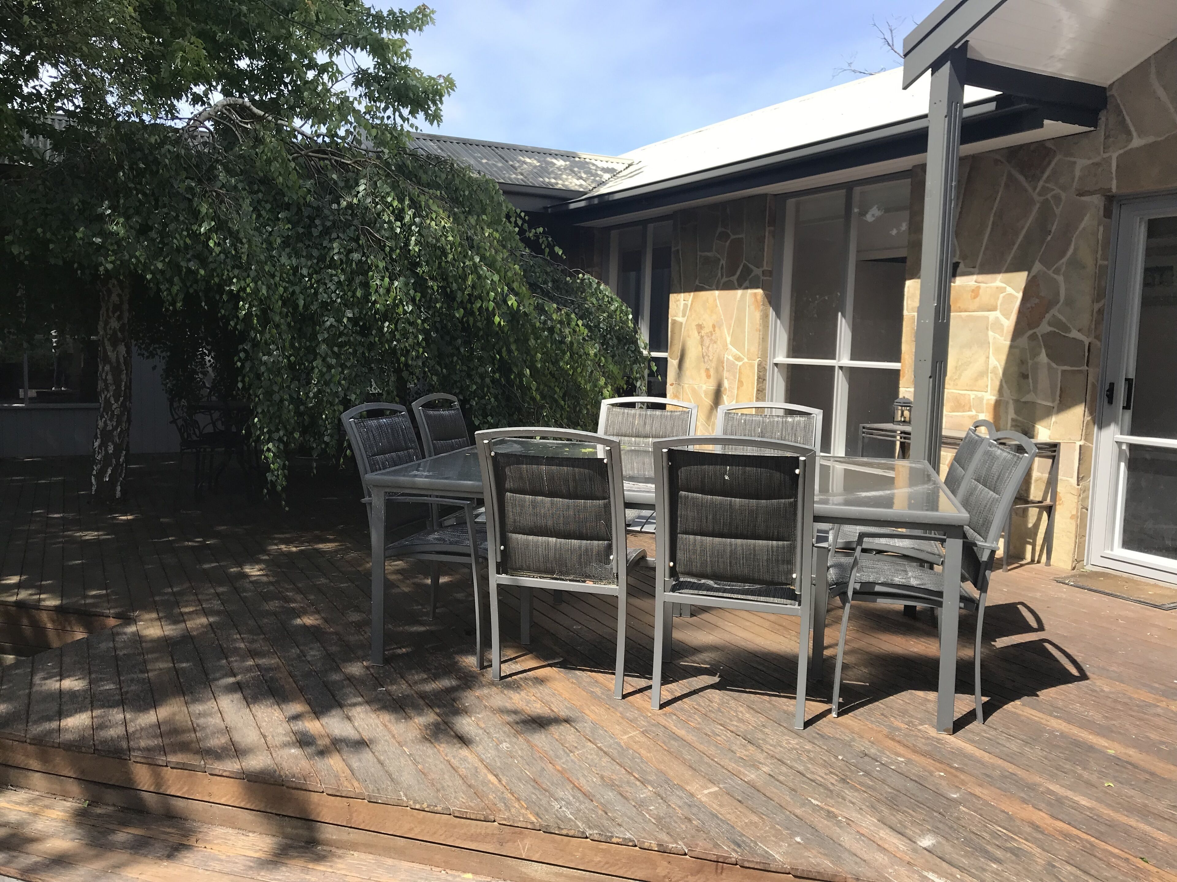 A patio with a table and chairs, a stone wall, and a tree.