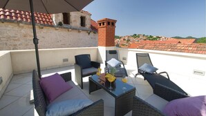 Terrassa al terrat amb mobles de vimet, una taula amb begudes i vista d'un edifici històric amb teules vermelles.