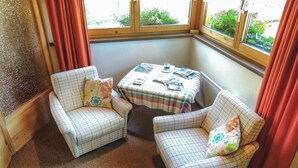 A corner room with two plaid armchairs, a small table with magazines, and a window with curtains. - Ferienwohnung in Obernberg (Obernberg)