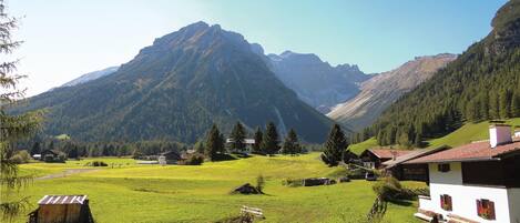 A rural mountain landscape with a white building featuring a red-tiled roof, surrounded by green fields and trees.