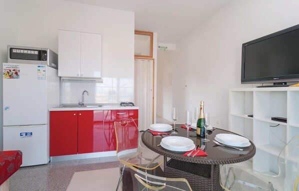 A compact kitchen with white cabinets, a red fridge, and a microwave. There's a dining table with plates, glasses, and a bottle. A TV is mounted on the wall. - Stunning home in Stomorska with sauna (Stomorska)