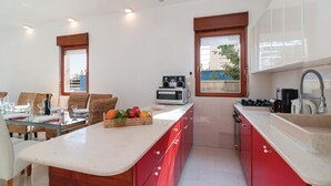 A modern kitchen with red cabinets, a microwave, and a sink. There is a dining area with wicker chairs and a glass table.