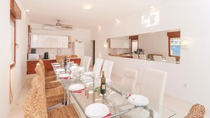 A modern dining area with a long table set for a meal, white chairs, and wicker baskets.