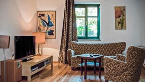 Una sala de estar con sofá, una mesita, televisor y ventana con cortinas.